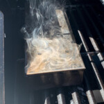 a smoker box with smoke coming out on the grates of a gas grill