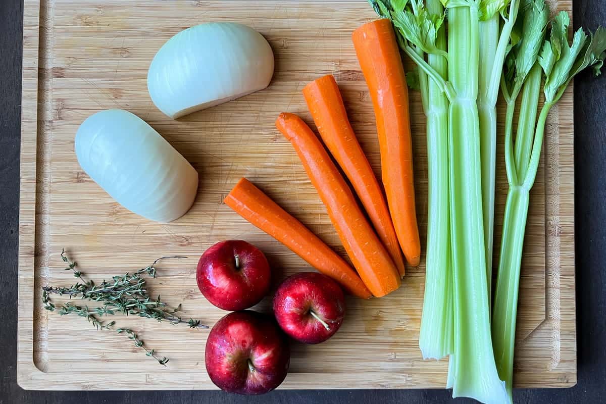 a cutting board with carrots, celery, onion, apples, and fresh thyme