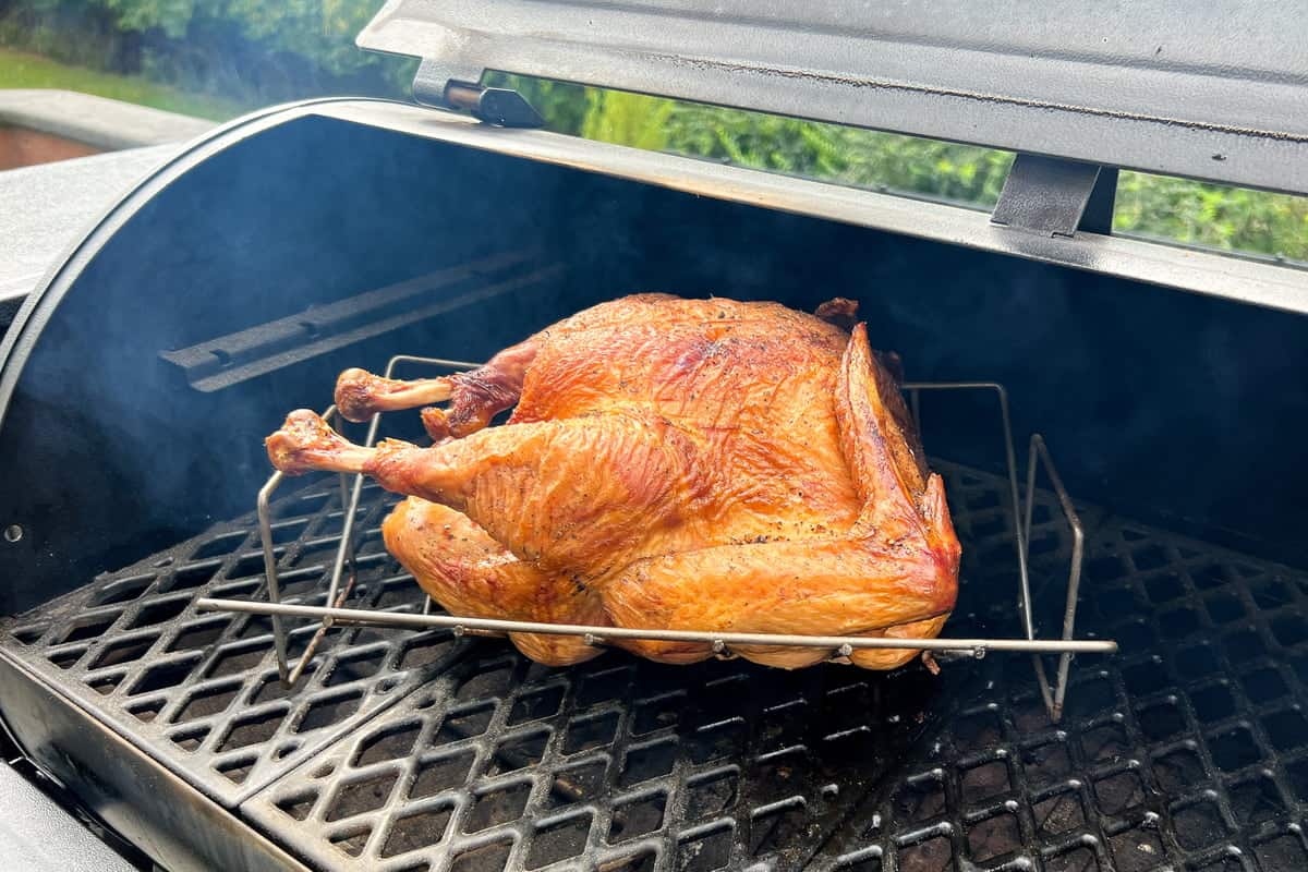 browned turkey on a v shaped rack on the grates of a pellet grill