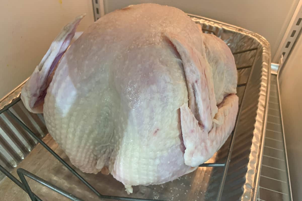 raw turkey on a rack in a foil pan in the refrigerator