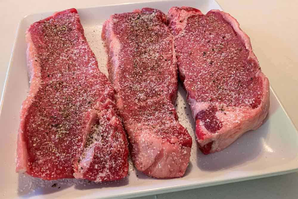 New York Strip steaks seasoned with salt and pepper on a plate