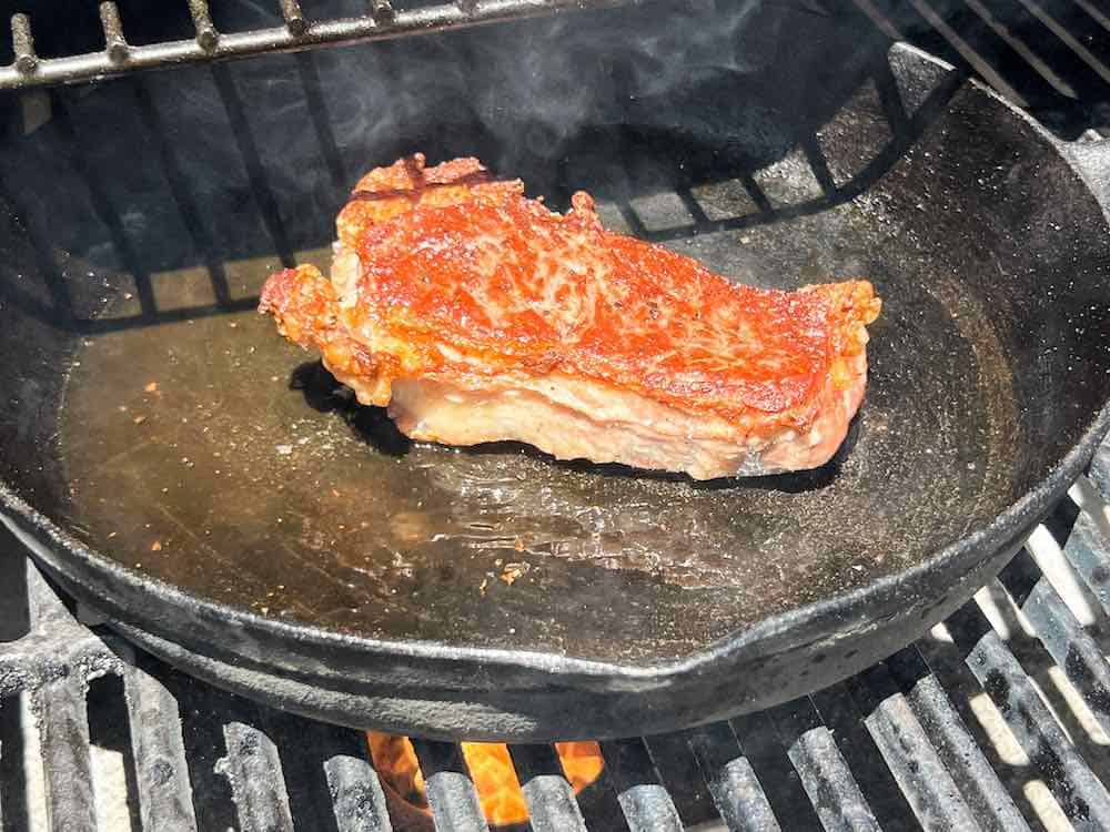 steak cooking in cast iron pan over direct heat on pellet grill