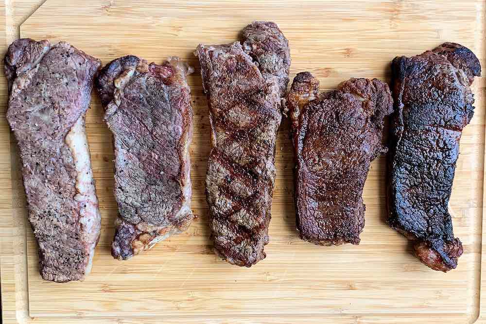 Cutting board showing comparison of 5 cooking styles for steaks all cooked to same internal temperature on a pellet grill