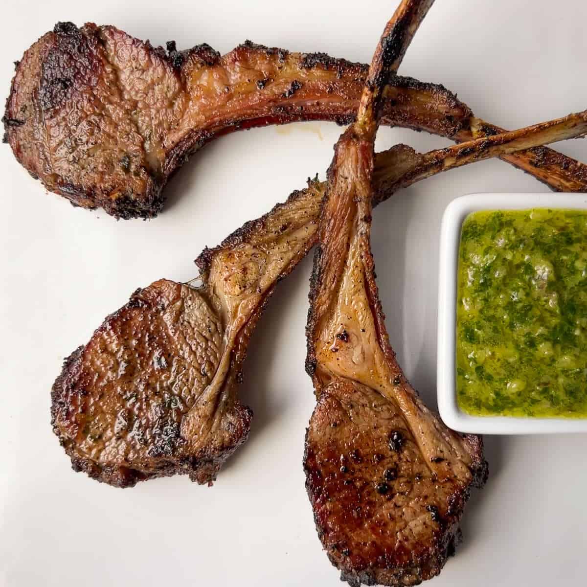 smoked lamb chops on a white plate with a white square dish of chimichurri sauce