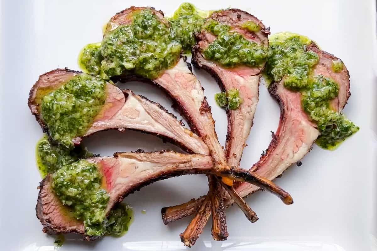 lamb chops arranged on a white plate with chimichurri sauce on each one