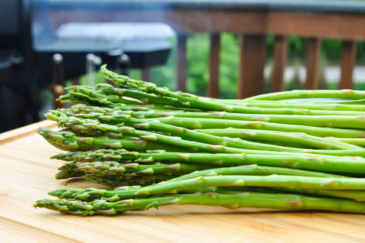 raw asparagus on a cutting board in front of a smoker