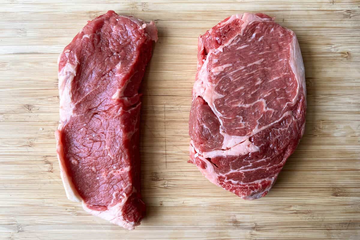 a New York Strip steak and a ribeye steak on a wooden cutting board