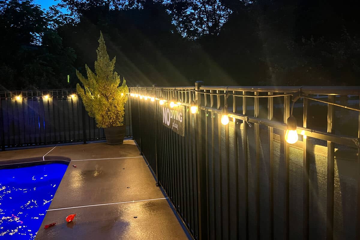 string lights on a fence surrounding an in ground pool