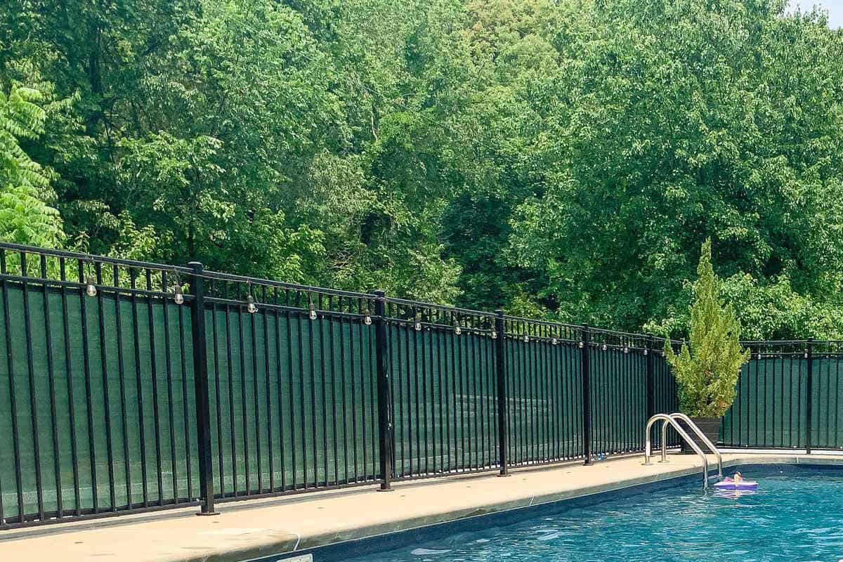 string lights hanging from a fence with zip ties with an in ground swimming pool near the fence