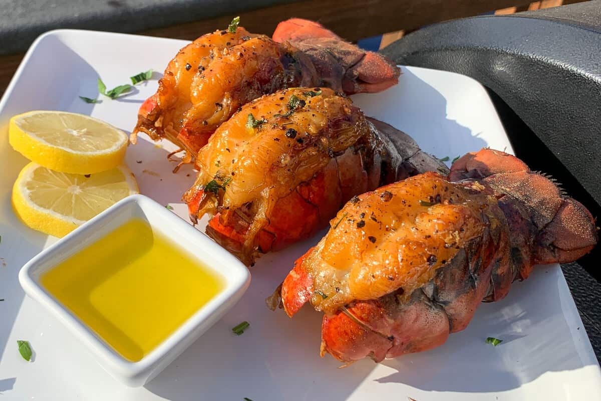 lobster tails on a white plate with a small dish of clarified butter and lemon slices