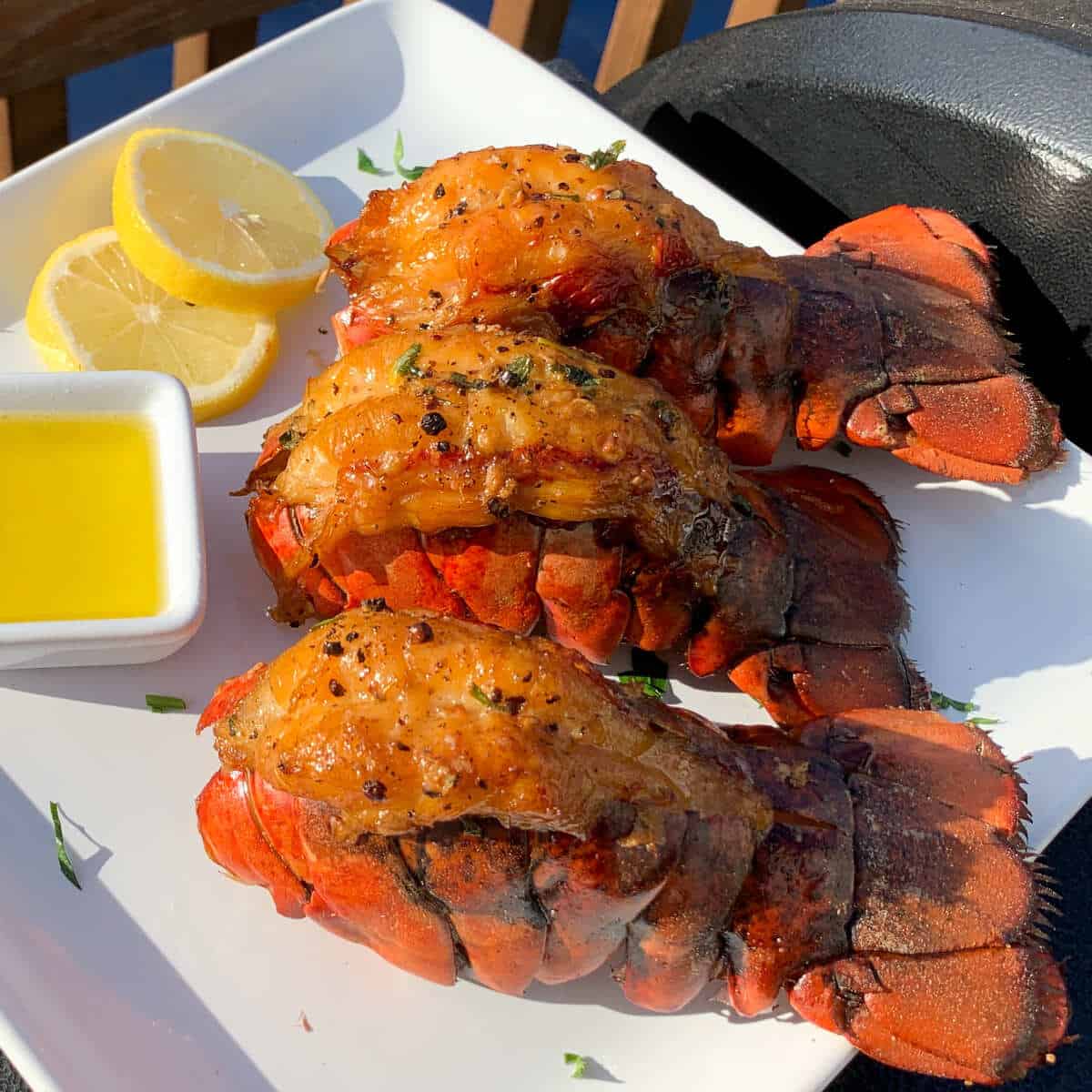 smoked lobster tails on a white plate with lemon slices and clarified butter