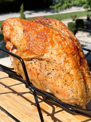 turkey breast cooked on a pellet grill on a metal rack set over a cutting board