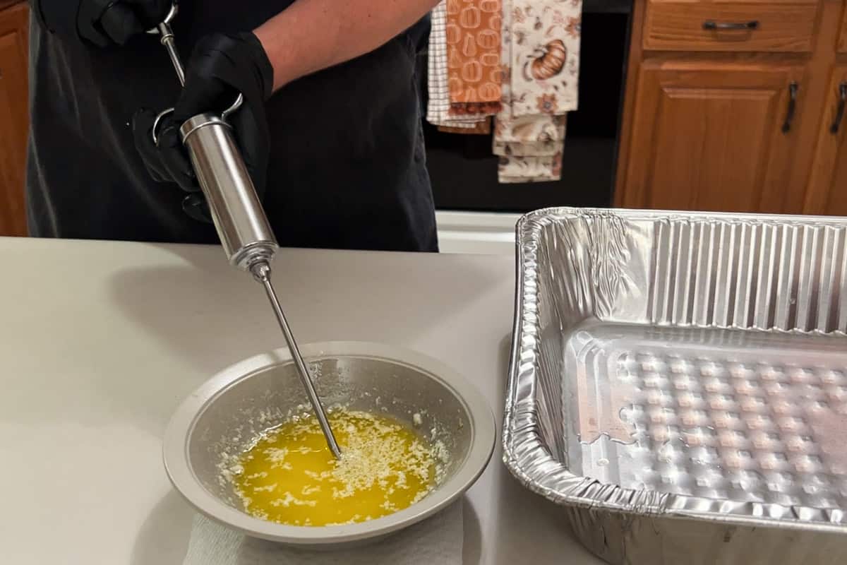 bowl of melted butter with a meat injector drawing the butter up