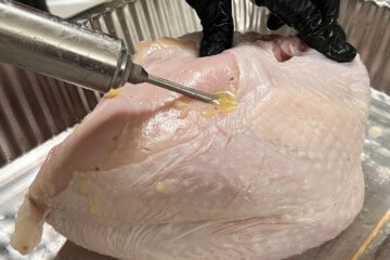 close up of a melted garlic butter being injected into a raw turkey breast