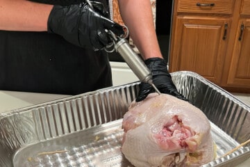 raw turkey breast in an aluminum foil pan being injected with butter using a meat injector