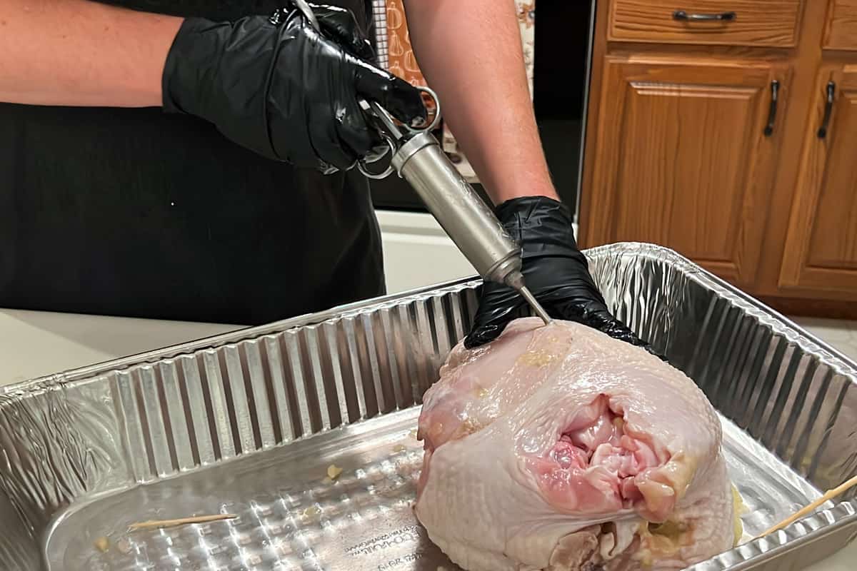raw turkey breast in an aluminum foil pan being injected with butter using a meat injector