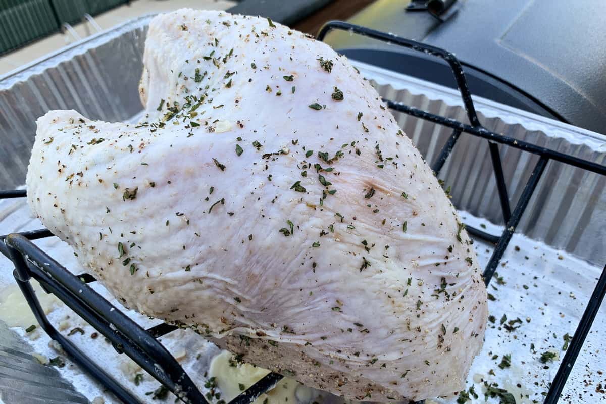 raw turkey breast seasoned with fresh sage and thyme in a v shaped rack set inside an aluminum foil pan