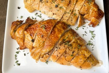 two turkey breasts on a white place sliced into thick slices and sprinkled with chopped fresh herbs