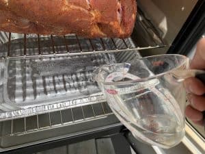 pouring water into the water pan of a masterbuilt electric smoker smoking a pork butt