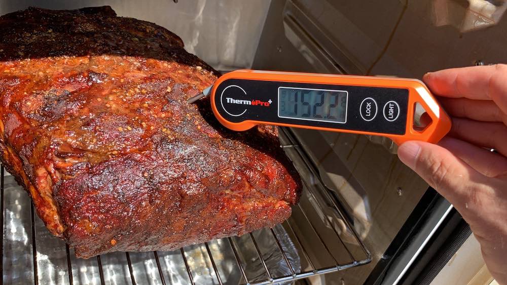 an instant read thermometer showing 150 degrees on a boston butt smoking in a masterbuilt electric smoker