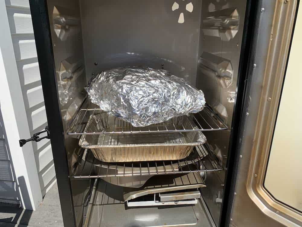 a wrapped pork butt placed in a masterbuilt electric smoker