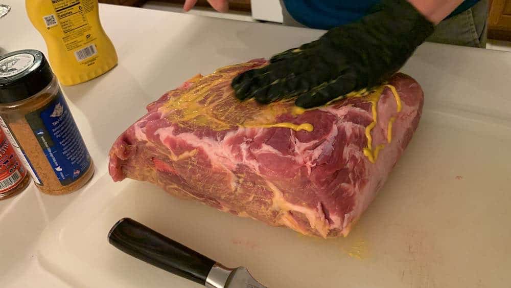 rubbing mustard on a raw pork butt