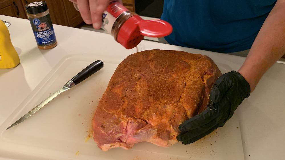 sprinkling seasoning on a raw pork shoulder