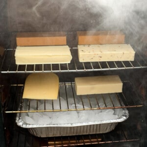 blocks of cheese smoking on the racks of a masterbuilt electric smoker with an ice pan below