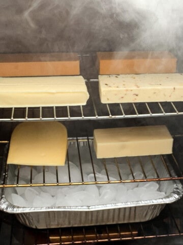 blocks of cheese smoking on the racks of a masterbuilt electric smoker with an ice pan below