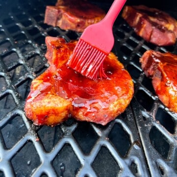 pork chop on the grates of a pit boss pellet grill being sauced with a silicone basting brush