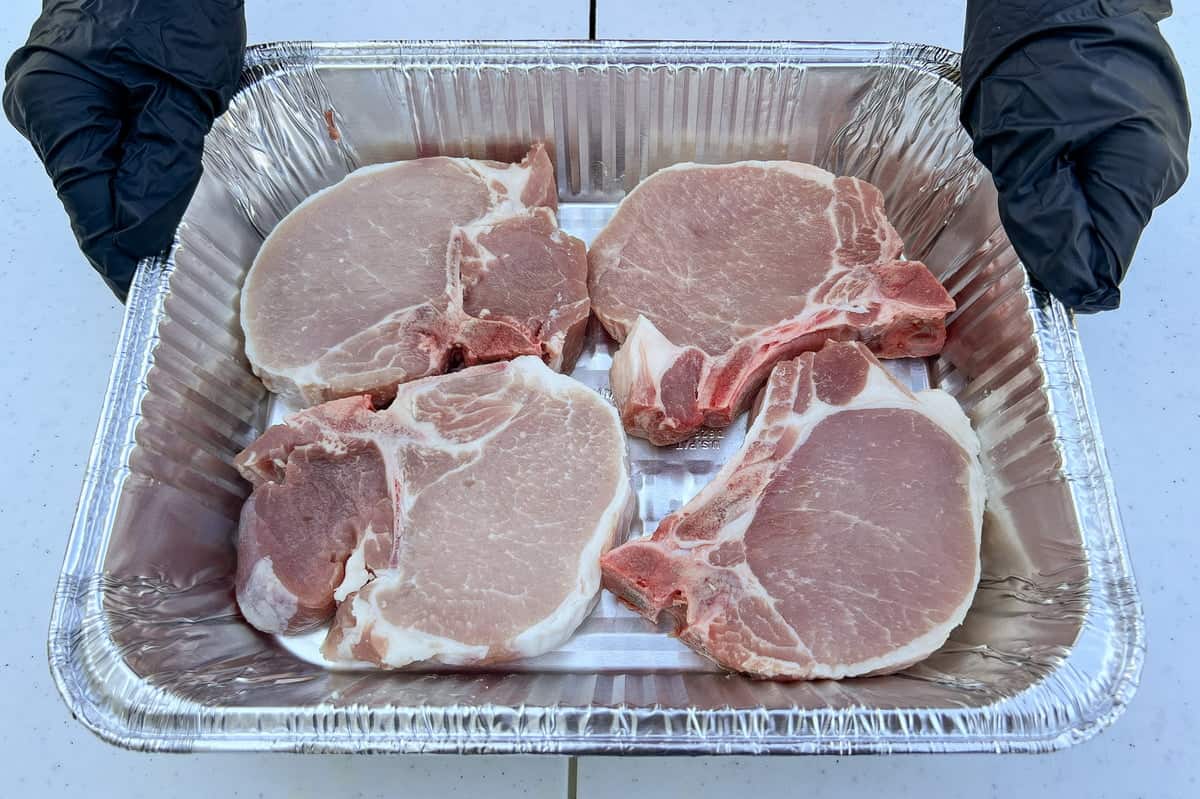 4 raw thick cut bone in pork chops in an aluminum foil pan