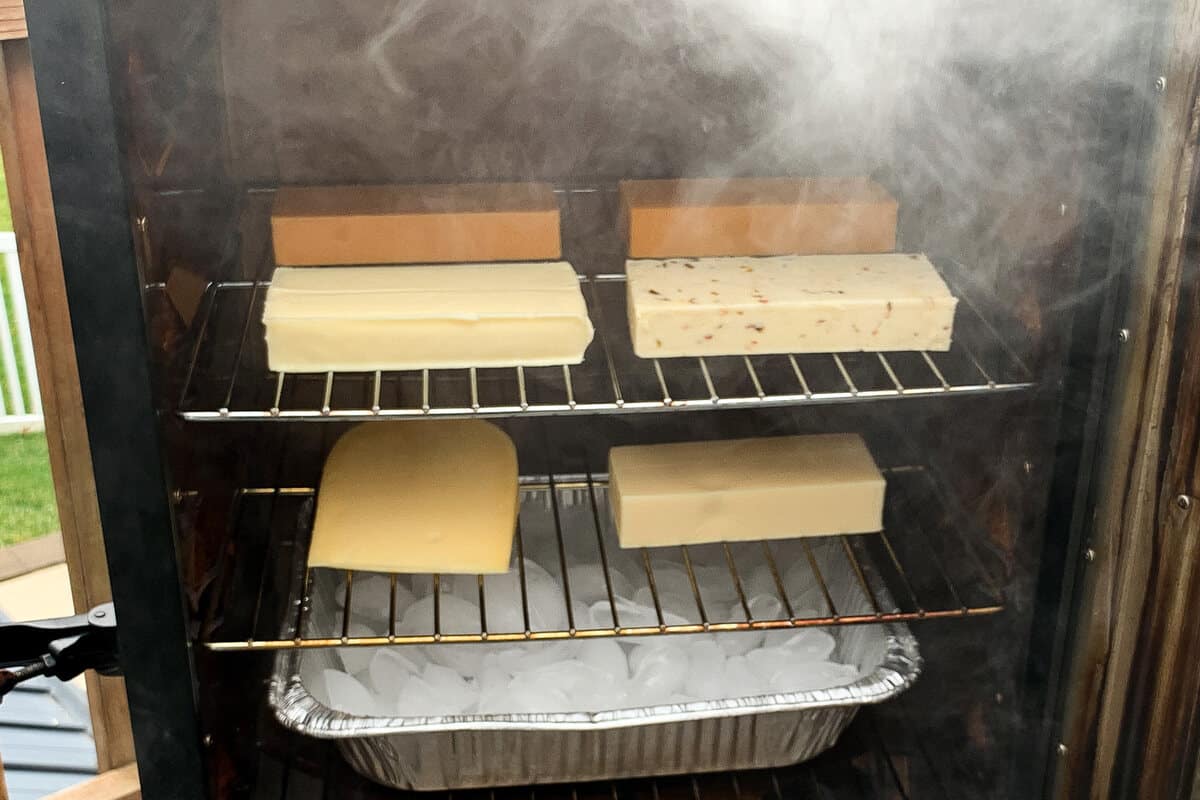 blocks of cheese smoking on the racks of a masterbuilt electric smoker with an ice pan below