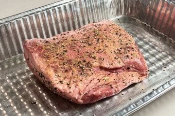 a raw corned beef brisket seasoned in an aluminum foil pan