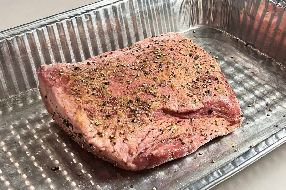 a raw corned beef brisket seasoned in an aluminum foil pan