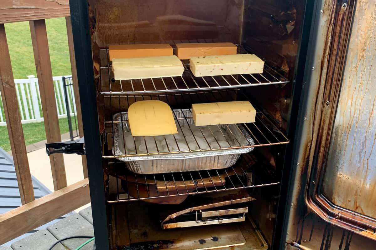 blocks of cheese on the racks of a masterbuilt electric smoker with an ice pan on the bottom shelf