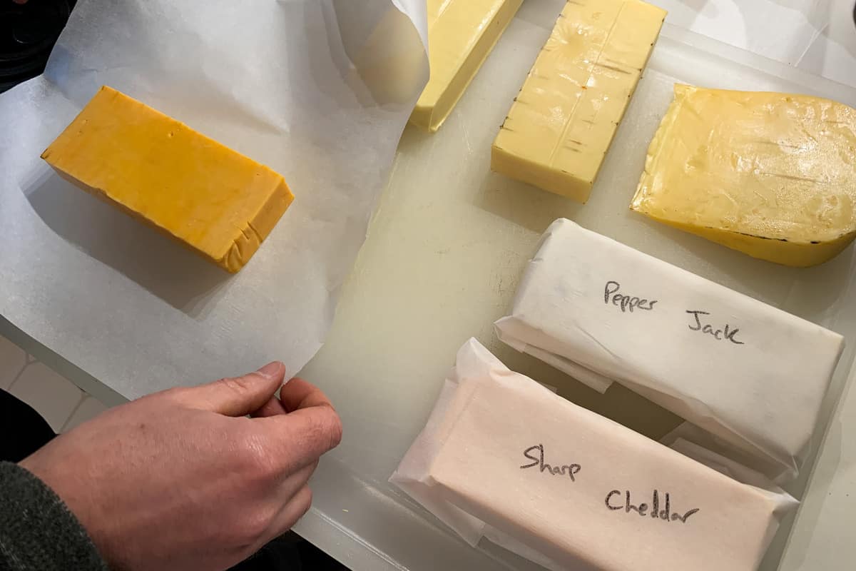 wrapping the blocks of cheese in parchment paper with two blocks wrapped and labeled