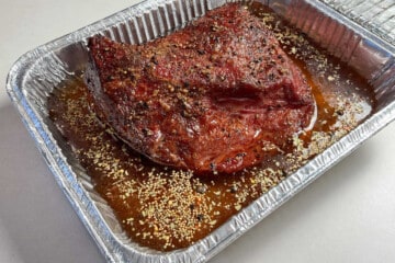 a corned beef brisket in an aluminum foil pan with beef broth and seasoning packet around it