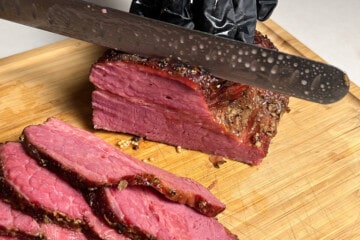 slicing a smoked corned beef brisket with a meat slicing knife on a wooden cutting board