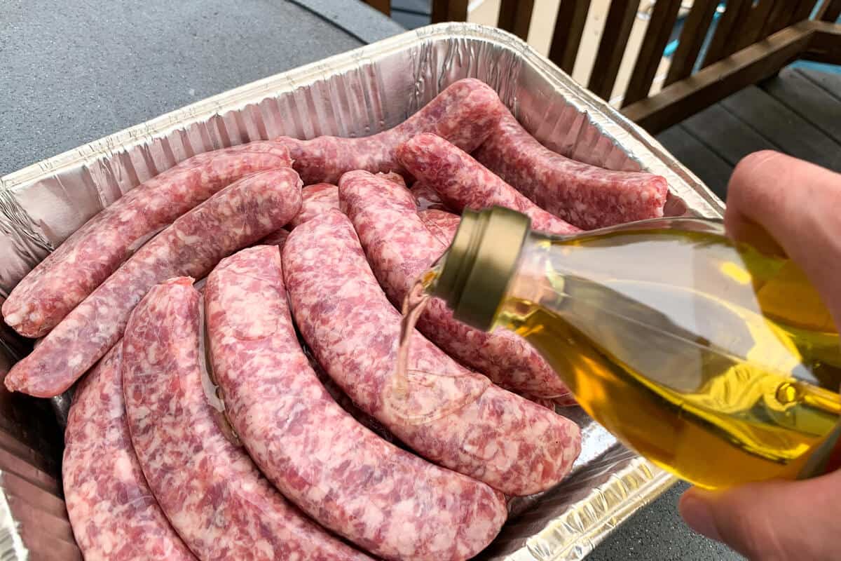 brats in a foil pan being oiled with olive oil