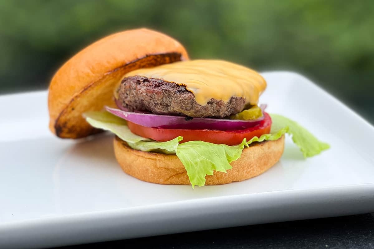 Pit Boss hamburger with cheese on a bun on a white plate with lettuce, tomato and red onion