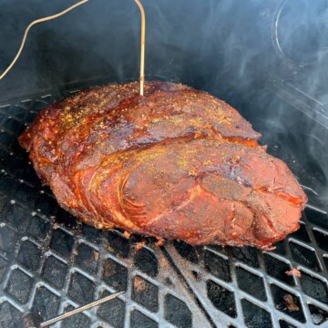pork shoulder on the grates of a pit boss pellet grill with a probe thermometer inserted in the meat