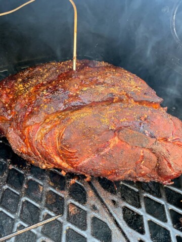 pork shoulder on the grates of a pit boss pellet grill with a probe thermometer inserted in the meat