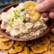 Smoked cream cheese dip in a bowl with some spread on a cracker and held up to show the dip