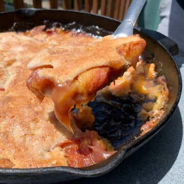 Smoked Peach Cobbler in a cast iron pan with some lifted up on a spoon to show the inside