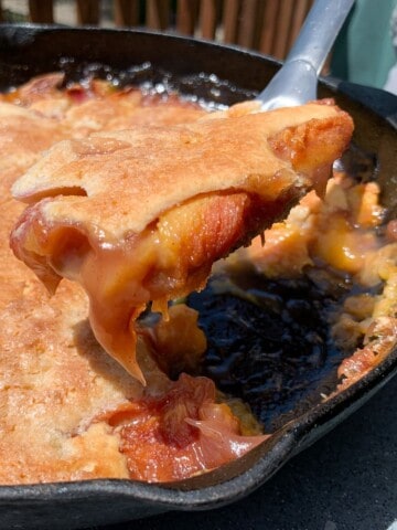 Smoked Peach Cobbler in a cast iron pan with some lifted up on a spoon to show the inside