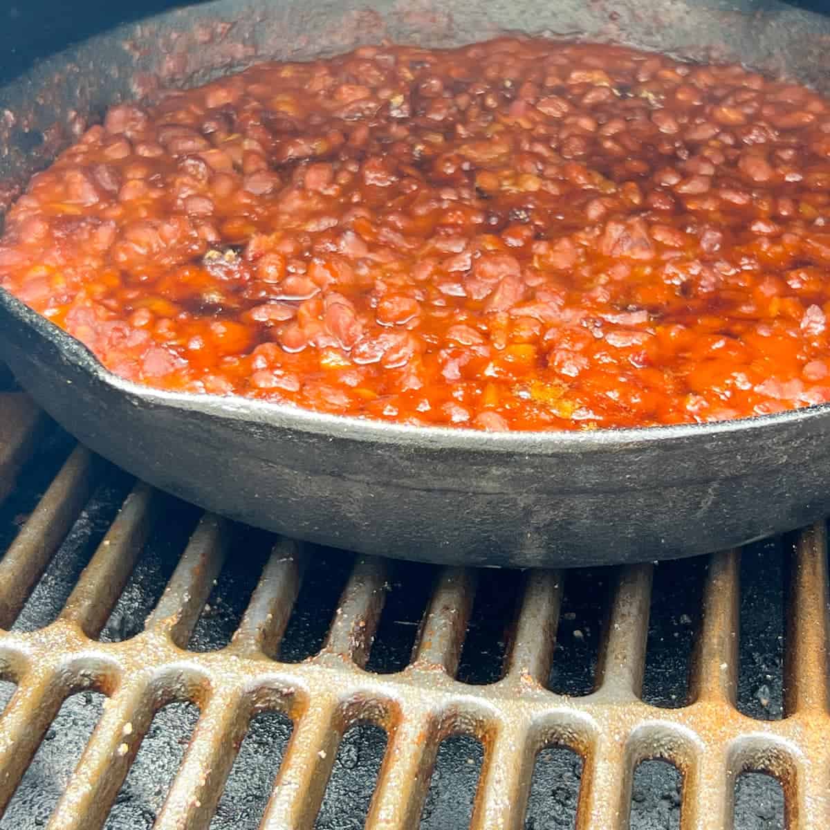 Baked beans in a cast iron skillet on the grates of a Traeger pellet grill