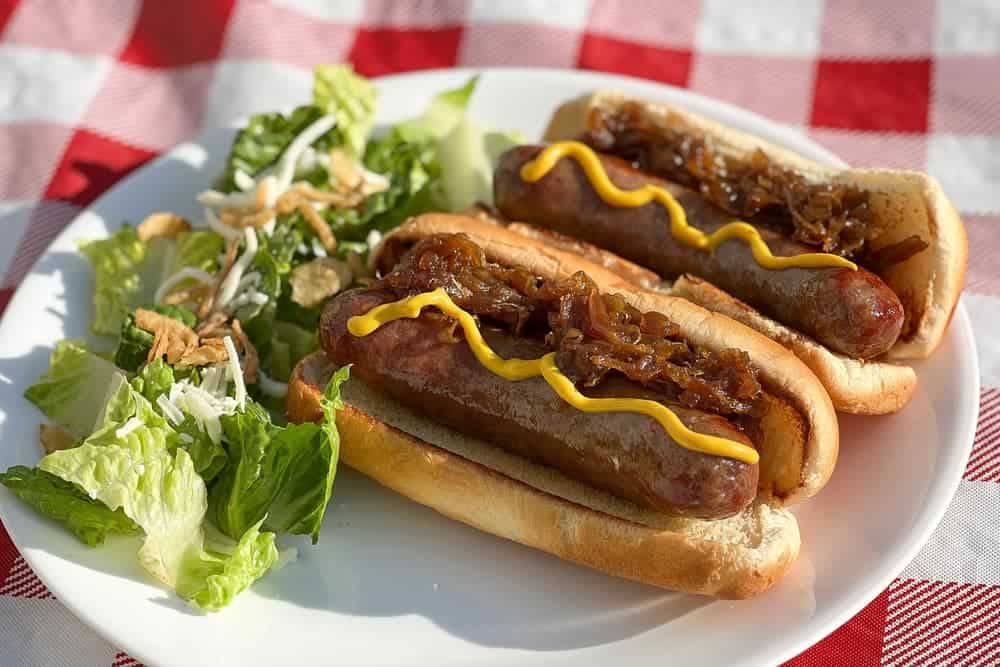 Bratwurst on Pellet Grill with caramelized onions on white plate with salad