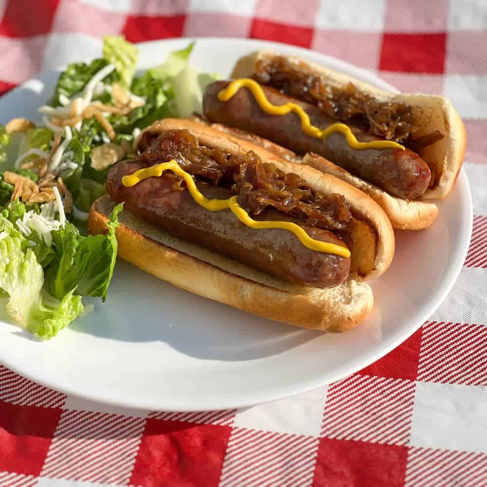 Bratwurst on Pellet Grill with caramelized onions on white plate with salad