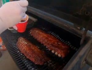 brushing bbq sauce on baby back ribs on a traeger pellet grill