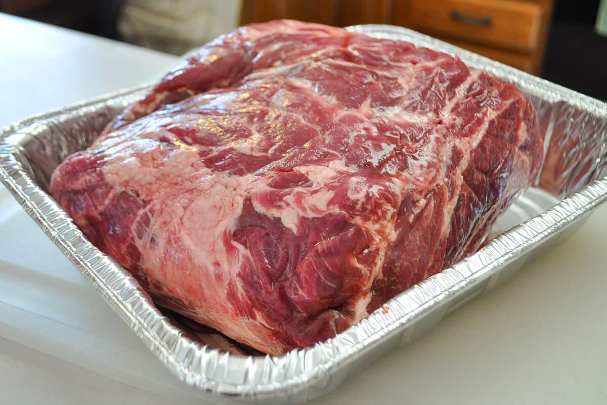 a raw pork shoulder in an aluminum foil pan on a counter